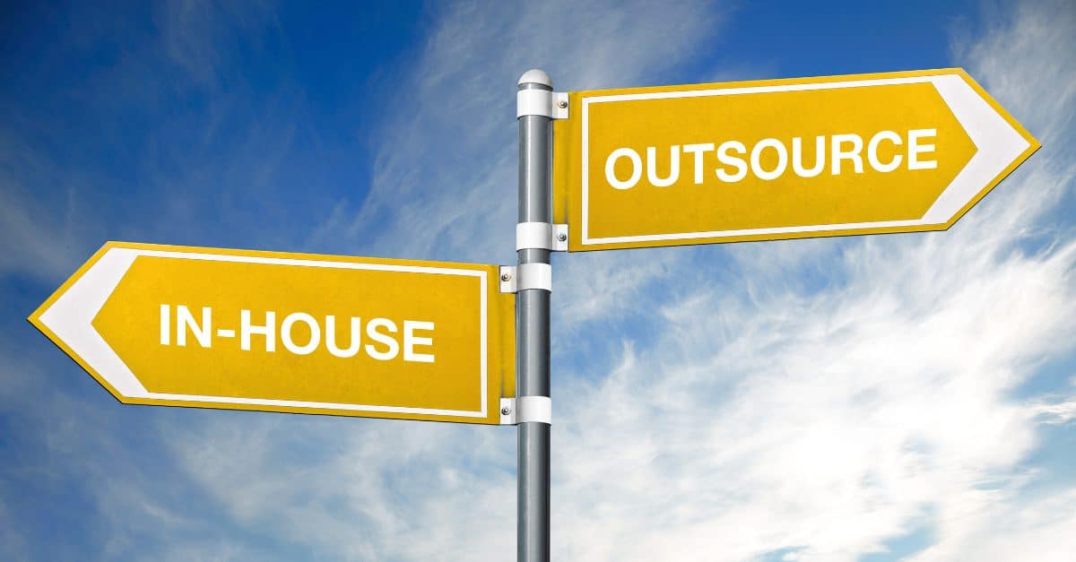 Yellow directional signs pointing to In-House and Outsource options against a blue sky, representing business decision-making choices